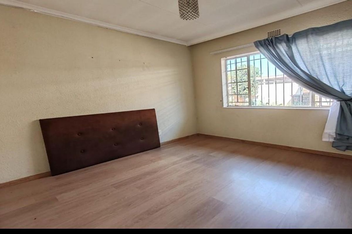A spacious bedroom featuring light-toned laminate flooring, security bars on the window, and neutral wall finishes, offering a blank canvas for personalization.