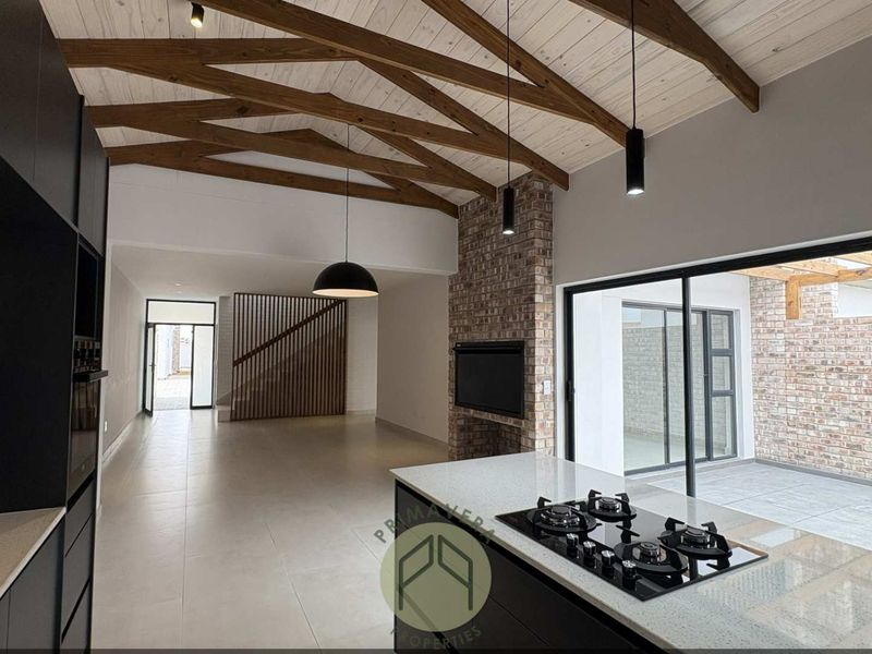 Spacious open-plan living area featuring exposed timber beams, a brick fireplace, and a modern kitchen with a central island and gas hob.