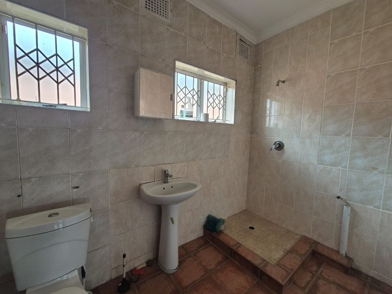 A functional bathroom featuring a pedestal basin, toilet, and a walk-in shower area with tiled finishes and security bars on the windows.