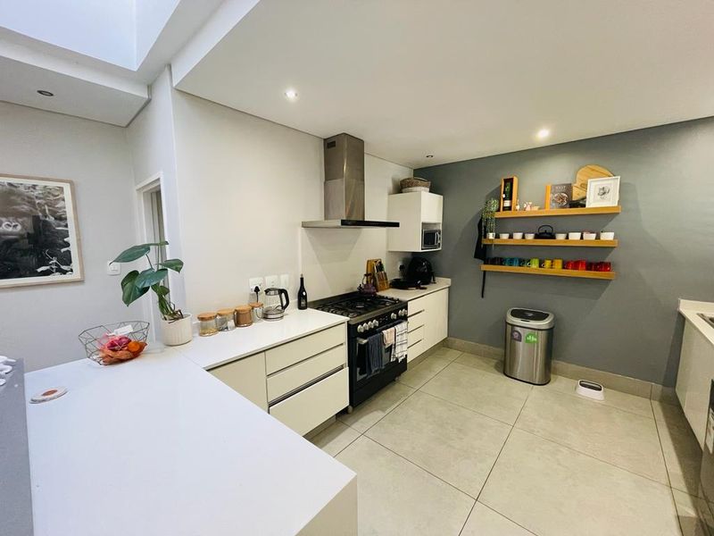 Modern kitchen featuring stone countertops, gas stove with extractor fan, ample cabinetry, and a bright skylight, finished with neutral tiled flooring.