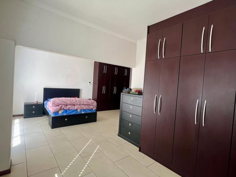 Spacious bedroom featuring extensive dark wood built-in cupboards and neutral tiled flooring, offering ample storage and a clean, functional layout.