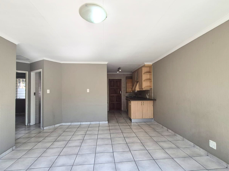 An open-plan living and kitchen area featuring neutral tiled flooring, built-in cabinetry, and a solid wood entrance door in a clean, vacant space.