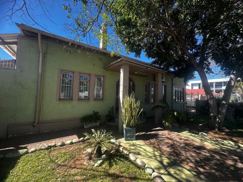 Front elevation of a mixed-use property featuring a covered entrance porch, paved driveway, and established garden area.