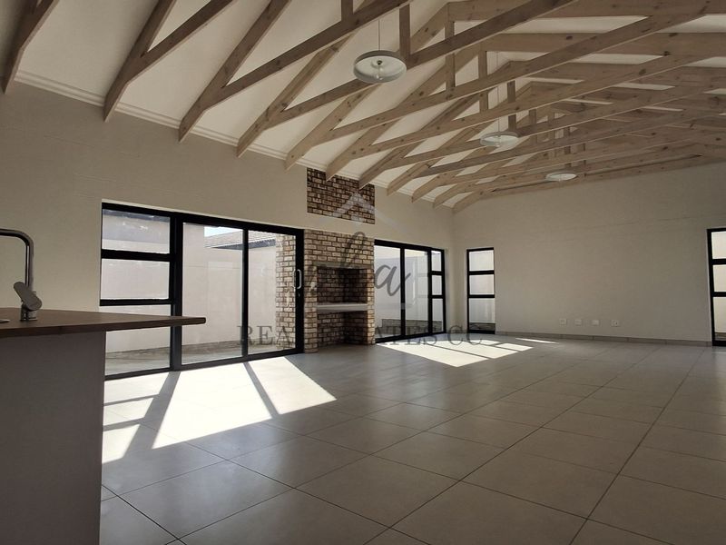 Spacious open-plan living area featuring exposed timber roof trusses, a brick fireplace, tiled flooring, and large aluminium sliding doors leading to the exterior.