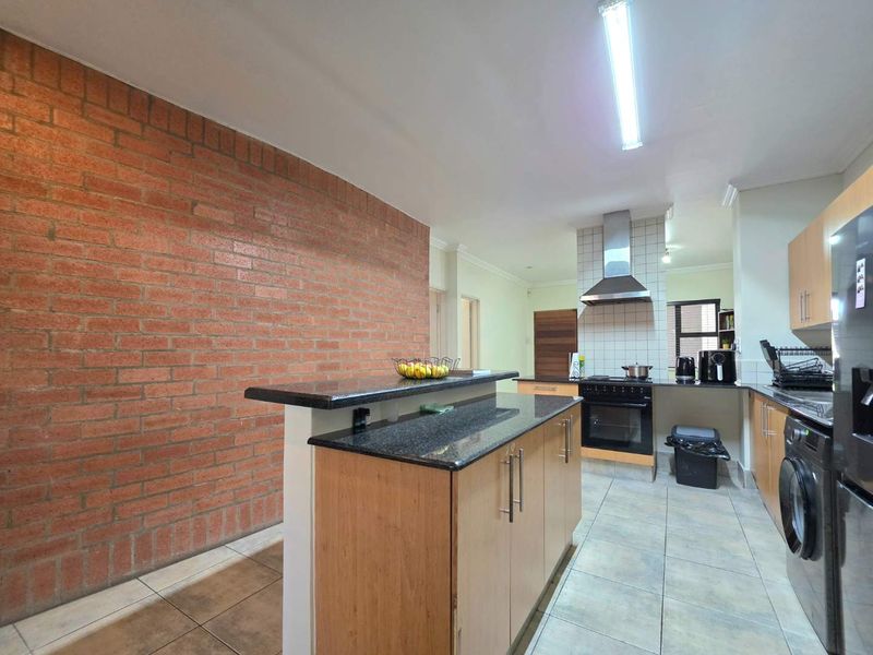 A functional kitchen featuring granite countertops, a breakfast bar, exposed brick wall, and built-in cabinetry with integrated oven and extractor fan.