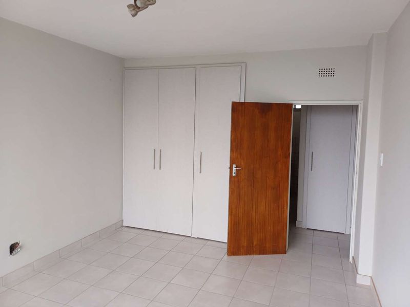 An empty bedroom featuring neutral tiled flooring, built-in white cupboards, and a wooden internal door.