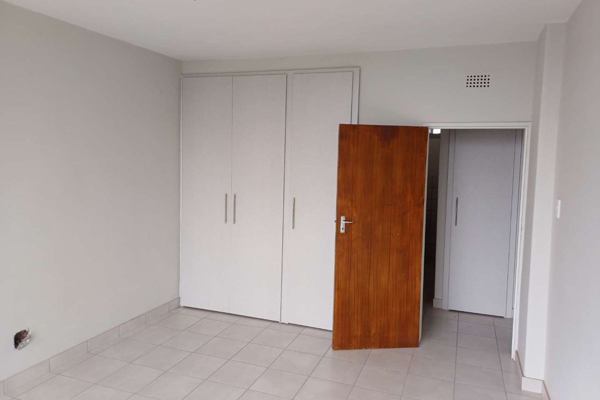 An empty bedroom featuring neutral tiled flooring, built-in white cupboards, and a wooden internal door.