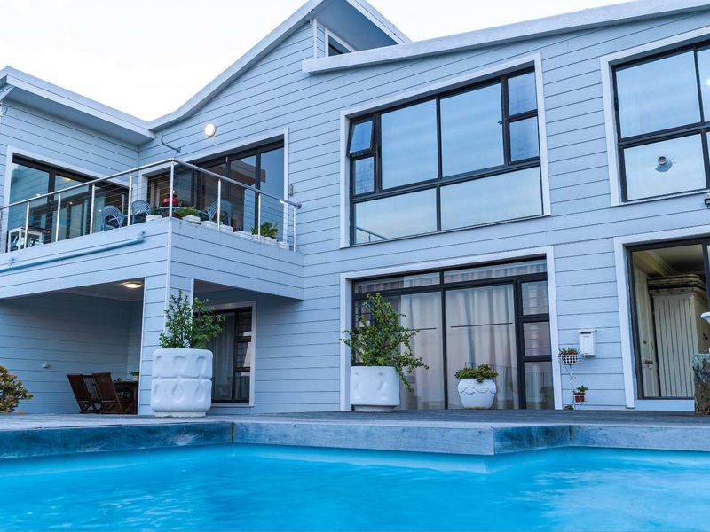 A modern two-story residence featuring a swimming pool, timber decking, and an elevated balcony with stainless steel balustrades.