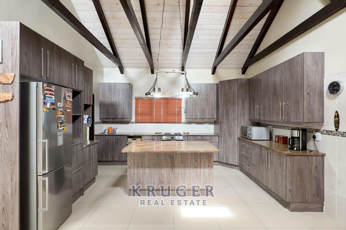 Spacious kitchen featuring wood-look cabinetry, granite countertops, a central island, and exposed timber ceiling beams.