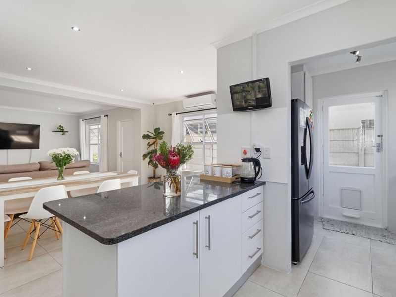 Modern open-plan kitchen and dining area featuring granite countertops, sleek cabinetry, tiled flooring, and recessed lighting, seamlessly flowing into the living space.