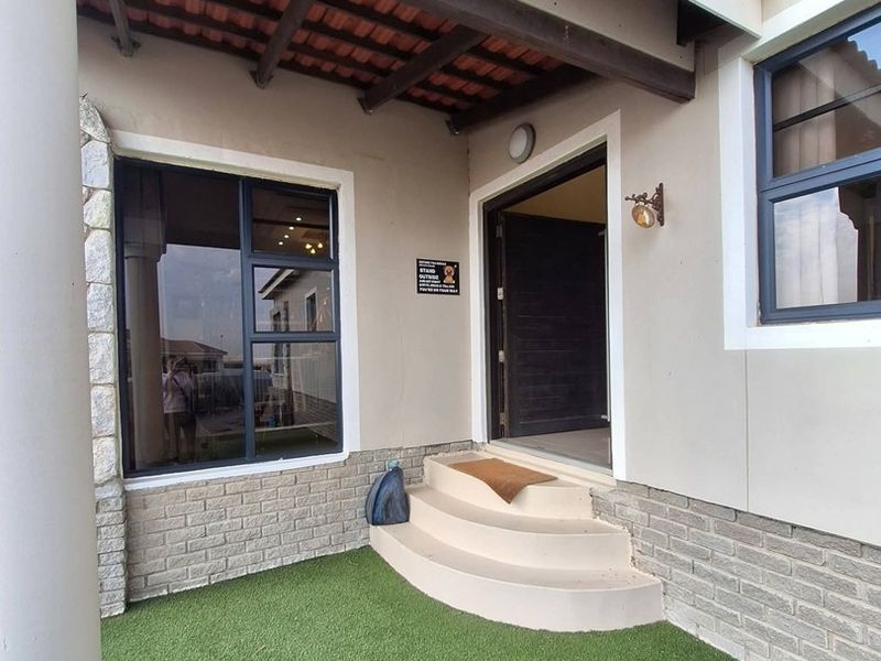 Front entrance area featuring a covered porch with exposed timber rafters, stone cladding accents, and a neat synthetic lawn.