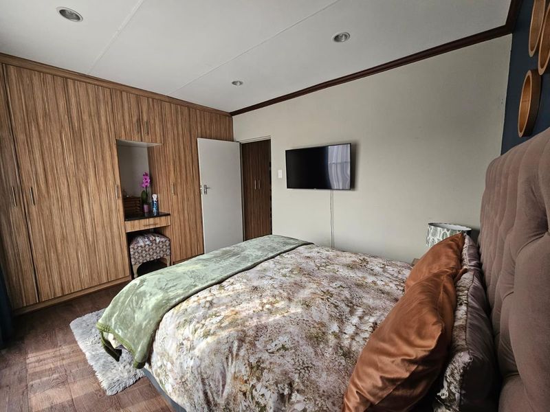 A well-maintained bedroom featuring extensive built-in wooden cabinetry with an integrated vanity nook, recessed ceiling lighting, and durable laminate flooring.