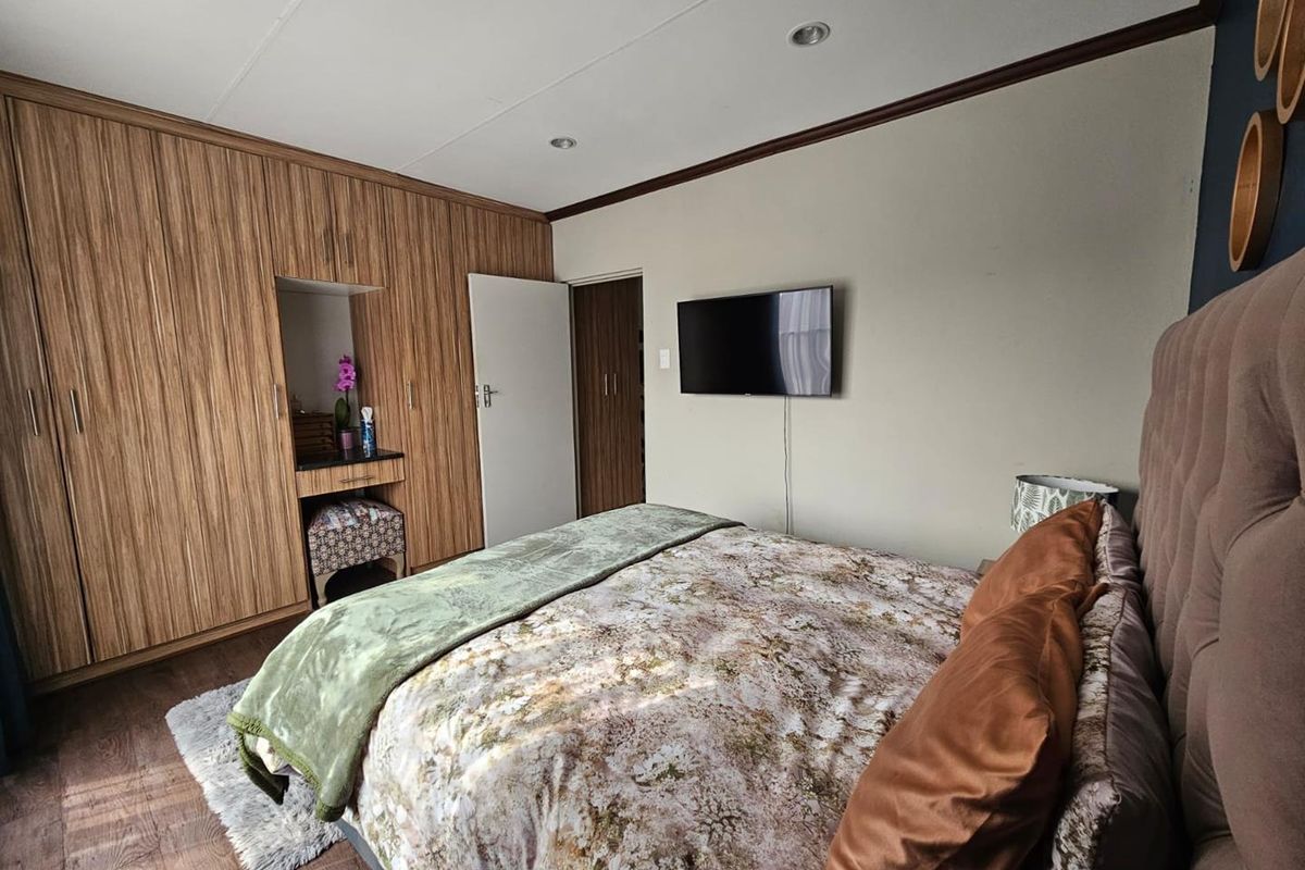 A well-maintained bedroom featuring extensive built-in wooden cabinetry with an integrated vanity nook, recessed ceiling lighting, and durable laminate flooring.