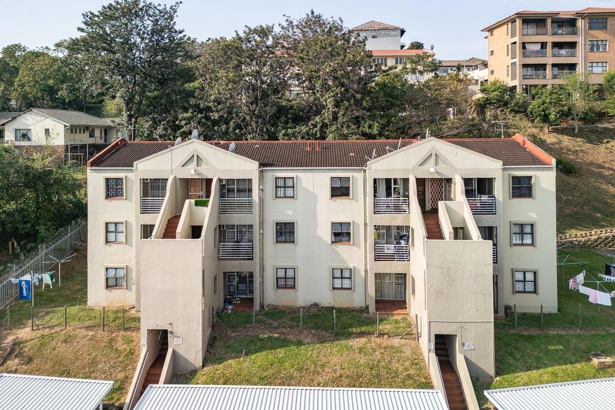 An elevated view of the rear facade of a multi-story apartment complex featuring external staircases, balconies, and associated parking carports.