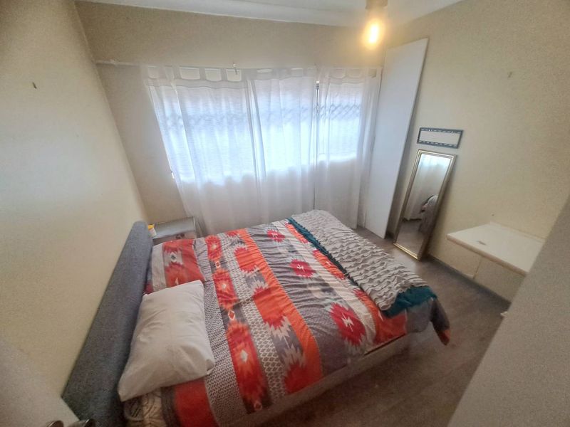 A compact bedroom featuring a built-in cupboard and large window, currently requiring cosmetic updates to the walls and flooring.