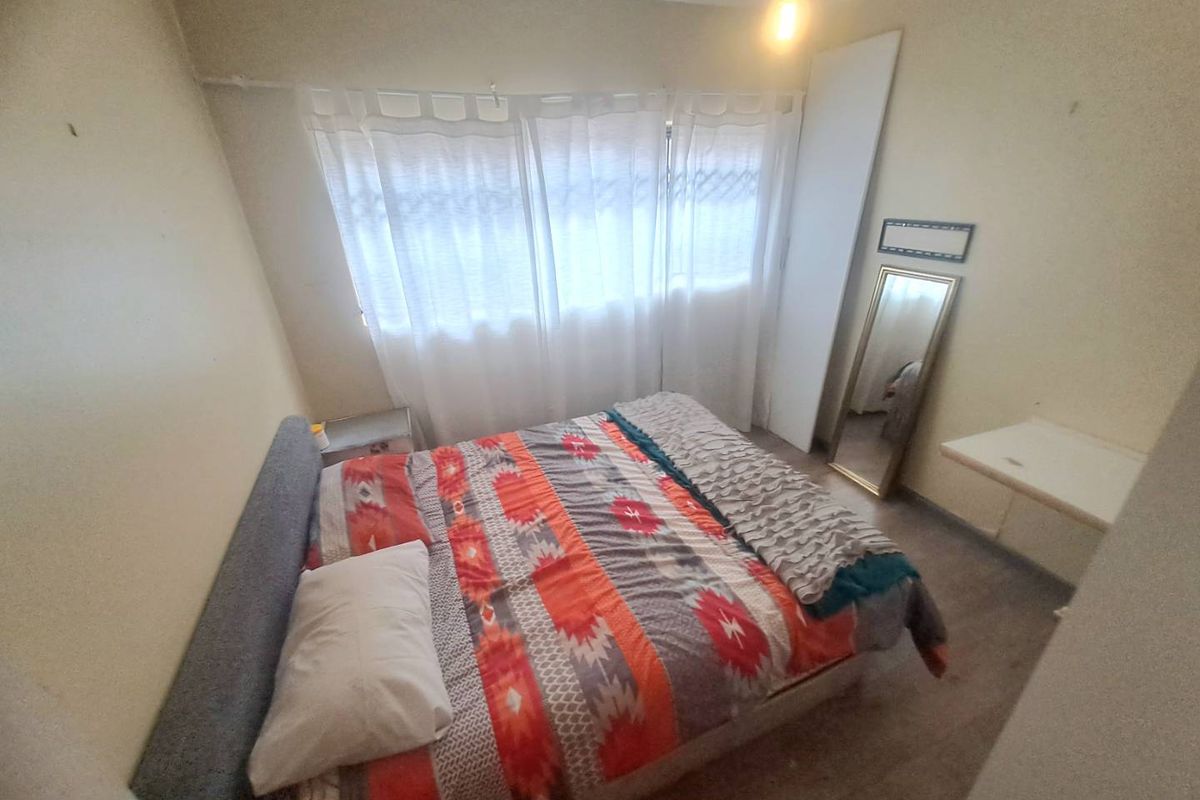 A compact bedroom featuring a built-in cupboard and large window, currently requiring cosmetic updates to the walls and flooring.