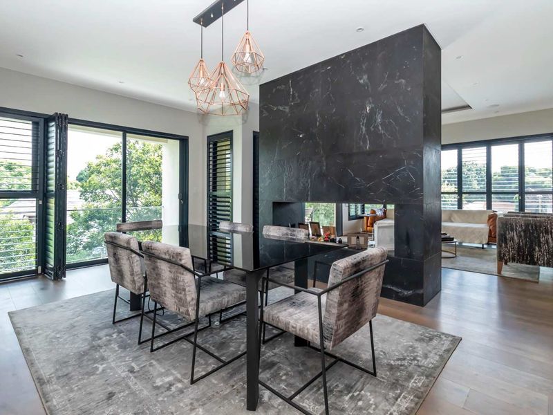 Spacious open-plan living and dining area featuring a striking double-sided black marble fireplace, timber flooring, and large bi-fold doors leading to a balcony.