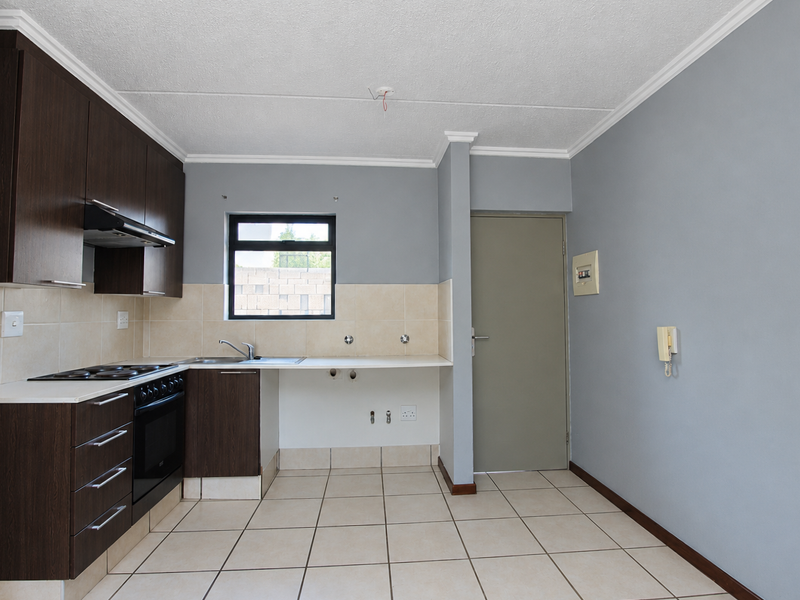 A functional kitchen featuring dark wood cabinetry, built-in oven, electric hob, and tiled flooring, offering a clean, blank canvas for potential updates.