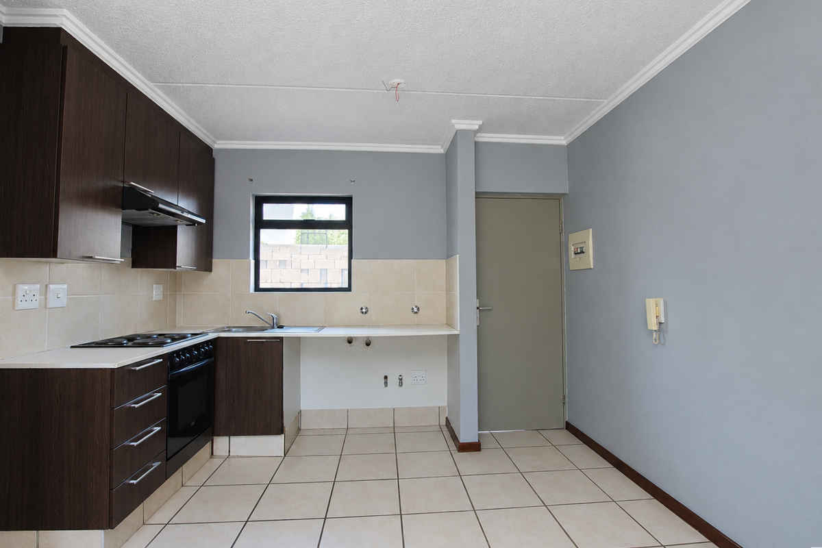 A functional kitchen featuring dark wood cabinetry, built-in oven, electric hob, and tiled flooring, offering a clean, blank canvas for potential updates.