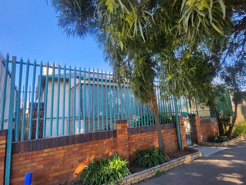 Front view of the property featuring a brick boundary wall with steel palisade fencing and a secure entrance gate.