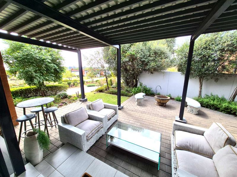 A spacious covered patio featuring paved flooring and a modern metal pergola, overlooking a private garden area.
