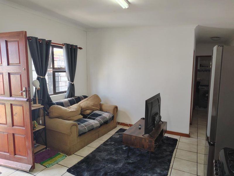 A compact living area featuring tiled flooring, a timber entrance door, and a window with security bars, leading through to a laundry area.