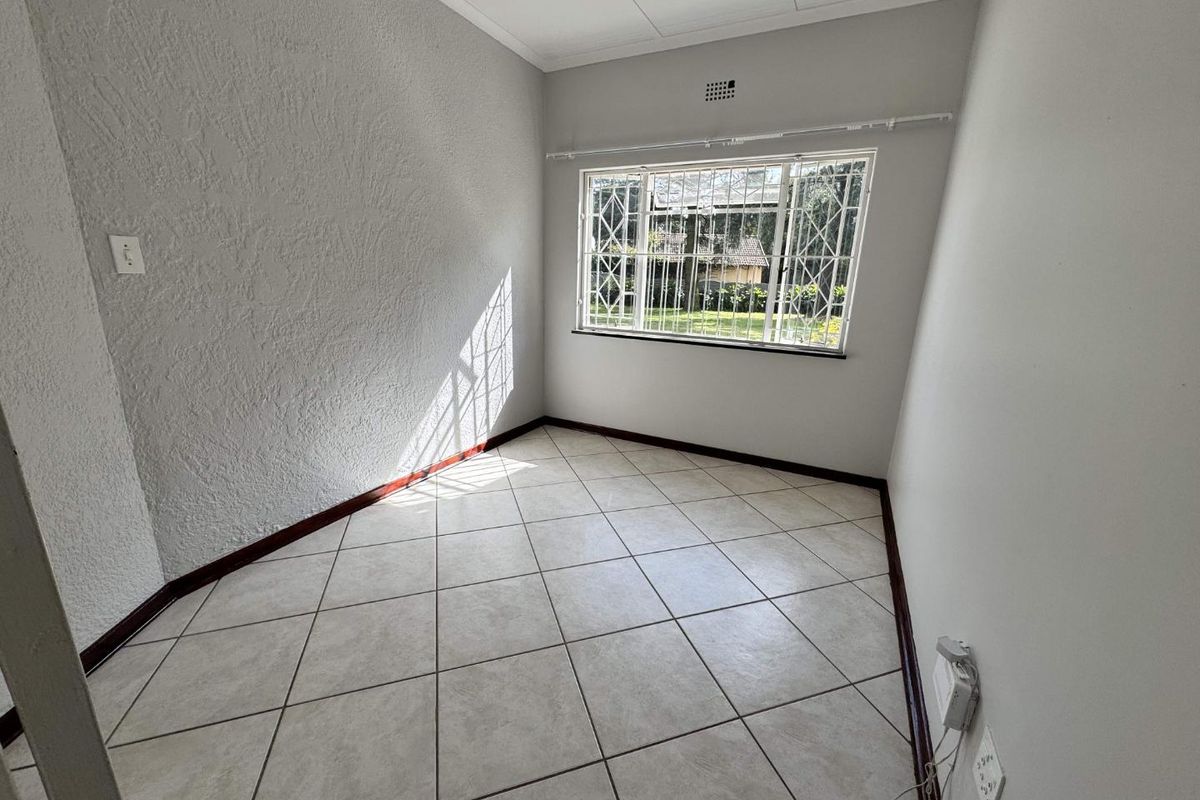 A bright, empty bedroom featuring neutral tiled flooring, textured walls, and a window fitted with security bars.