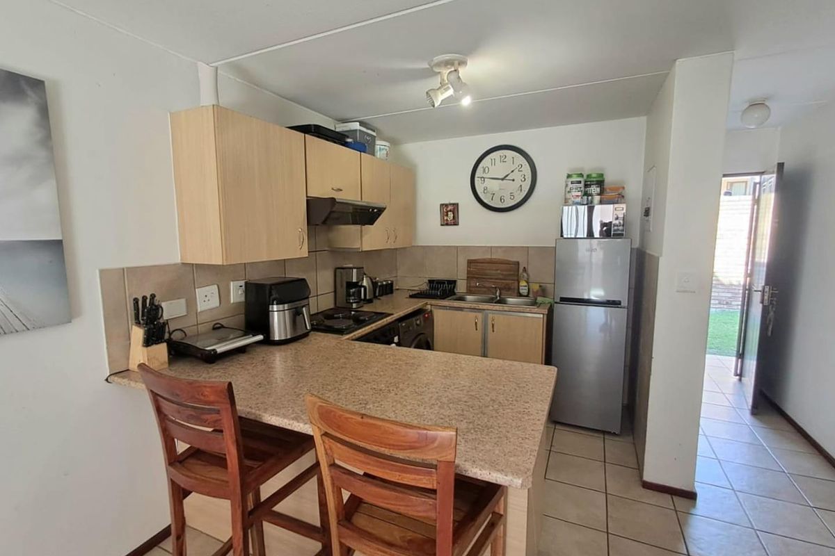 Compact kitchen featuring laminate countertops, built-in cabinetry, a breakfast bar, and tiled flooring, with direct access to an outdoor area.