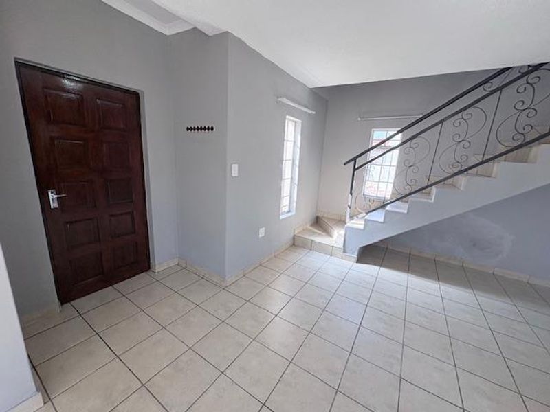 An empty entrance hall featuring tiled flooring, a solid wood front door, and a staircase with a decorative wrought iron balustrade.