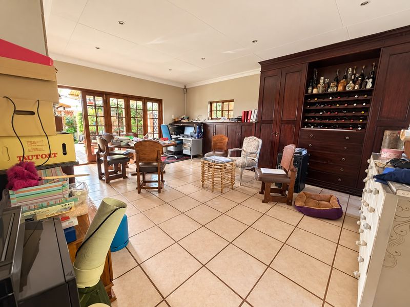 Spacious living area featuring extensive built-in cabinetry with integrated wine storage, tiled flooring, and direct access to the outdoor patio through wooden doors.
