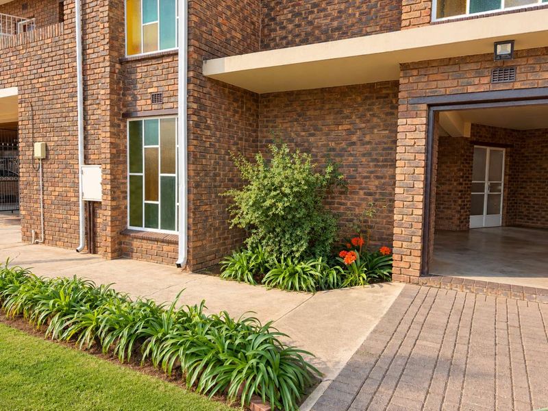 A well-maintained apartment exterior featuring a classic face brick facade, paved driveway, and neat garden landscaping with concrete walkways.