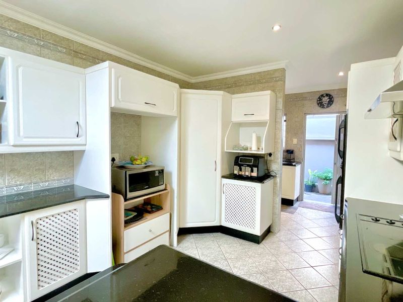 A functional kitchen featuring white cabinetry, dark granite countertops, tiled flooring, and a tiled backsplash, with an adjacent scullery area visible.