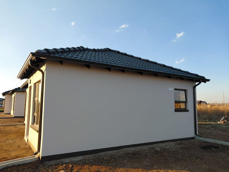 A view of the rear exterior of a modern house featuring a tiled roof, plastered walls, and aluminium window frames.
