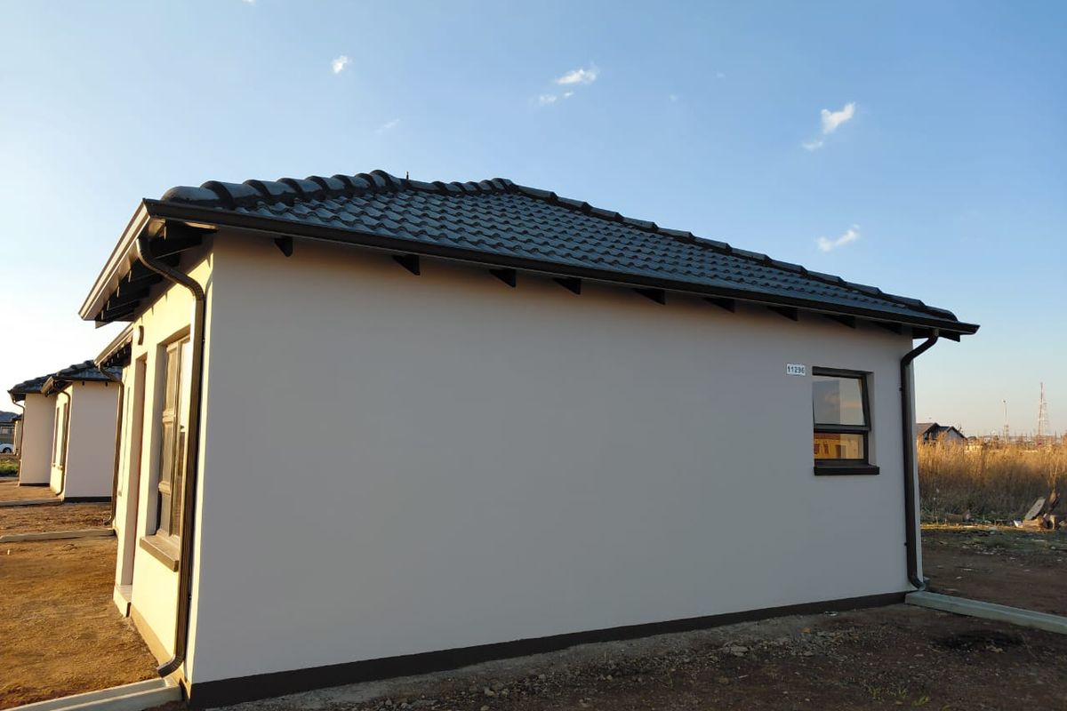 A view of the rear exterior of a modern house featuring a tiled roof, plastered walls, and aluminium window frames.