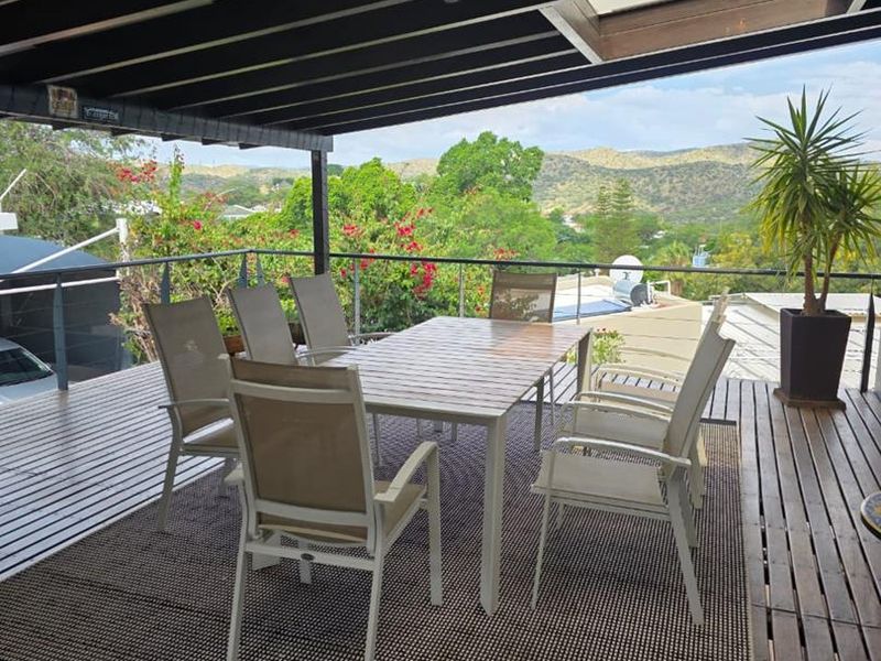 A spacious covered timber deck balcony featuring a pergola with skylights, metal railings, and elevated views of the surrounding landscape.