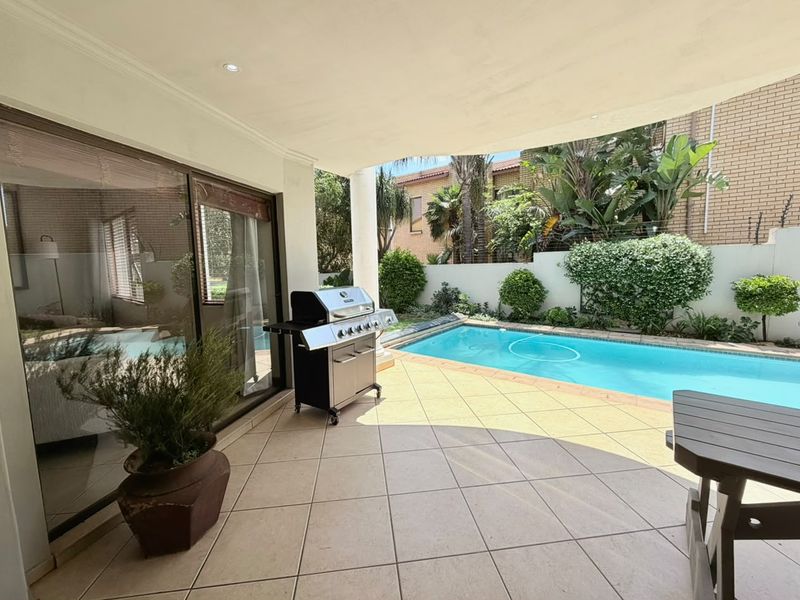Covered patio area featuring tiled flooring and recessed lighting, providing direct access to the swimming pool and landscaped garden.