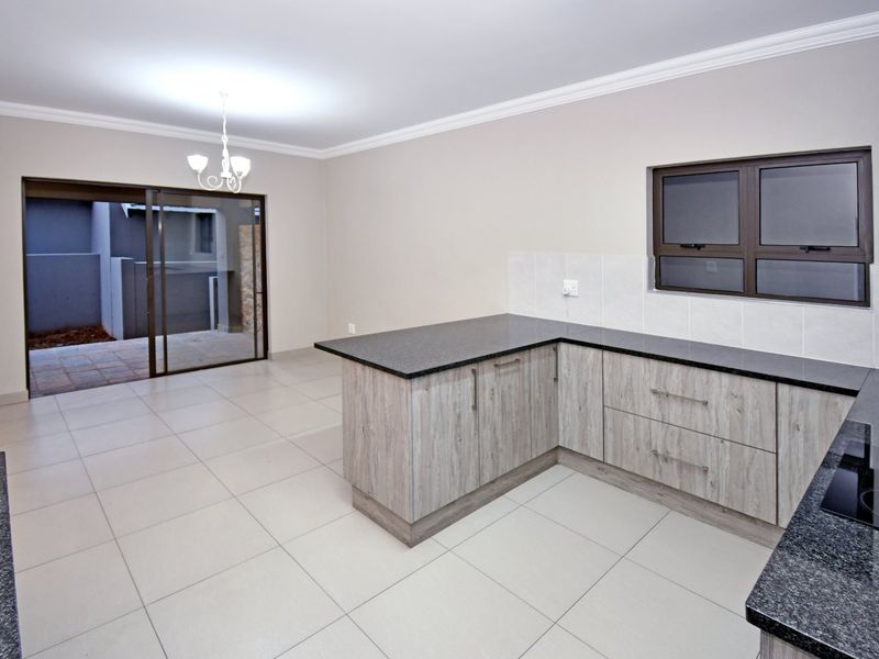 An open-plan kitchen and living area featuring modern wood-look cabinetry, granite countertops, tiled flooring, and direct access to an outdoor patio through sliding doors.