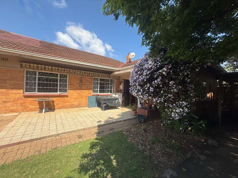 Rear view of a brick house featuring a paved patio area, security-barred windows, and a tiled roof.