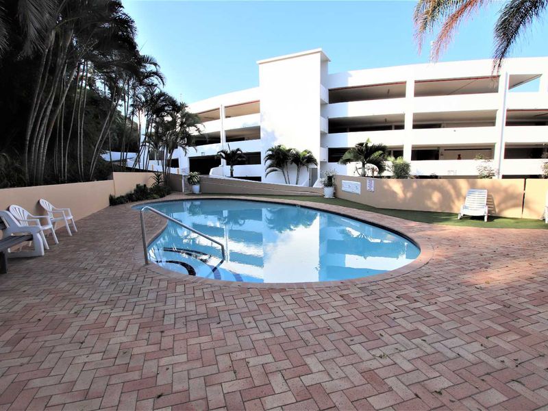 A communal swimming pool area featuring brick paving, a boundary wall, and a metal handrail, set within a well-maintained townhouse complex.