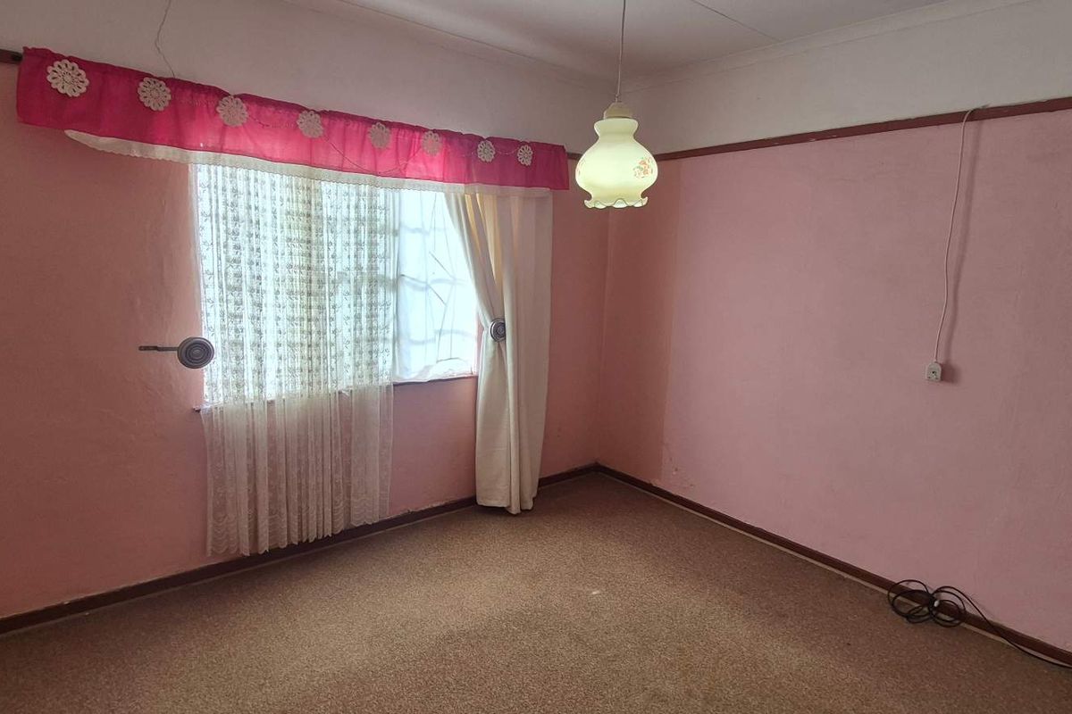 A bedroom featuring pink walls, carpeted flooring, and a central pendant light fixture, offering a blank canvas for potential renovation and modernization.