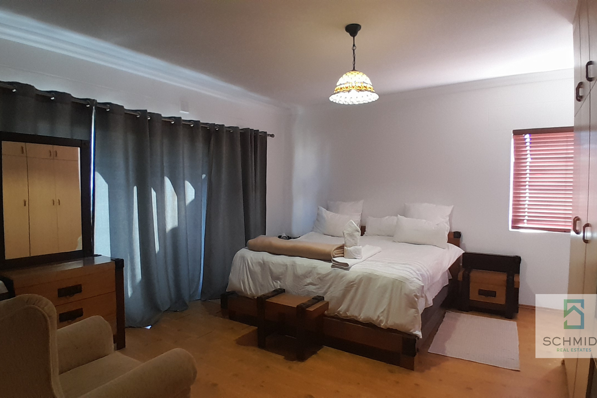 Spacious bedroom featuring built-in cupboards, neutral walls, and large windows with blinds and curtains, providing a comfortable and functional living space.