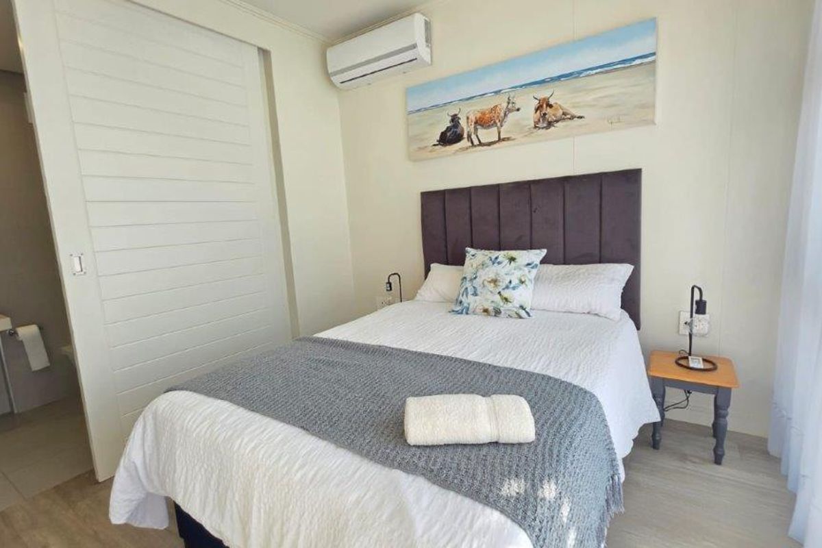 A well-maintained bedroom featuring laminate flooring, a wall-mounted air conditioning unit, and direct access to an en-suite bathroom.