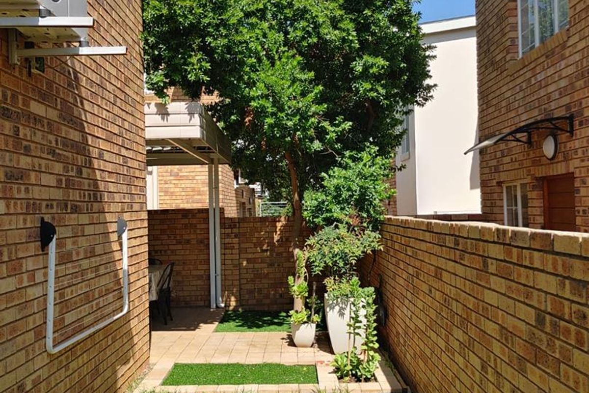 A private rear courtyard featuring face brick walls, a paved patio area, and a small lawn, providing a low-maintenance outdoor space.