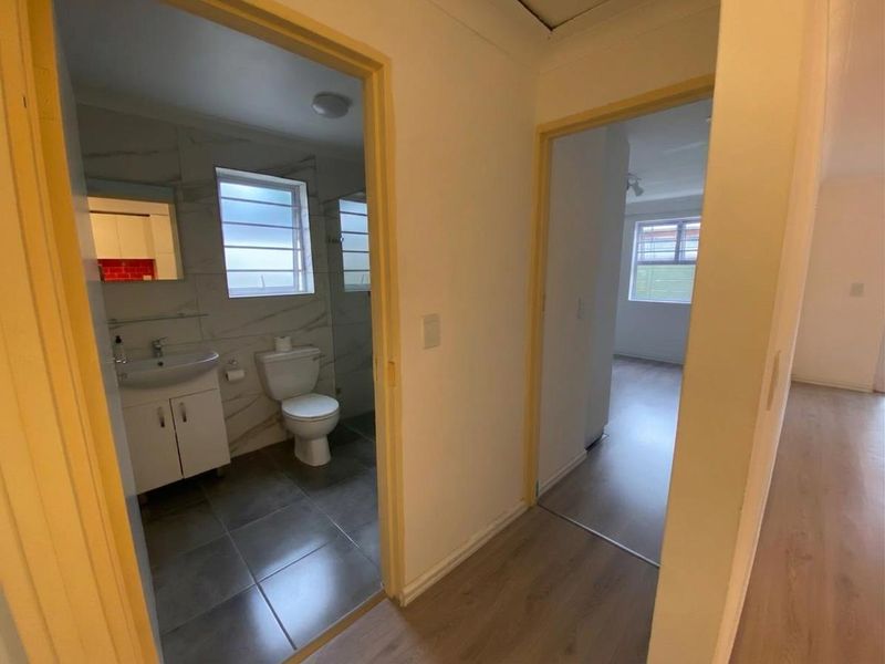 A view from the hallway looking into a modernised bathroom with tiled finishes and a separate bedroom area with laminate flooring.