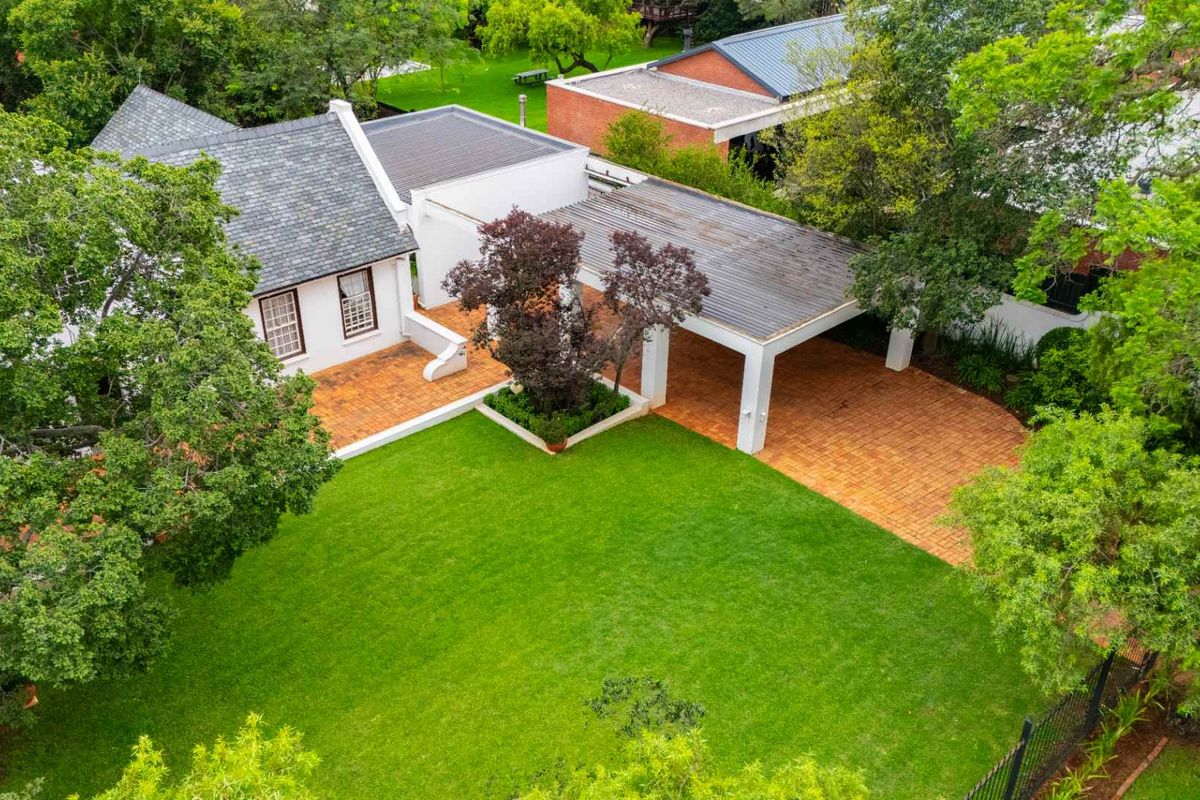 Aerial view of the property featuring a well-maintained garden, brick paved driveway, covered carport, and a tiled roof structure.