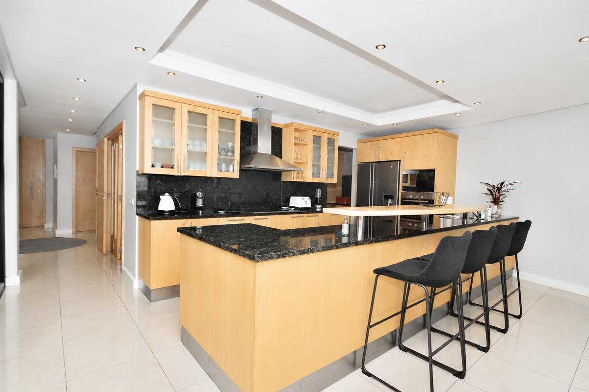 Modern kitchen featuring light wood cabinetry, dark granite countertops, a breakfast bar, and integrated stainless steel appliances with recessed ceiling lighting.