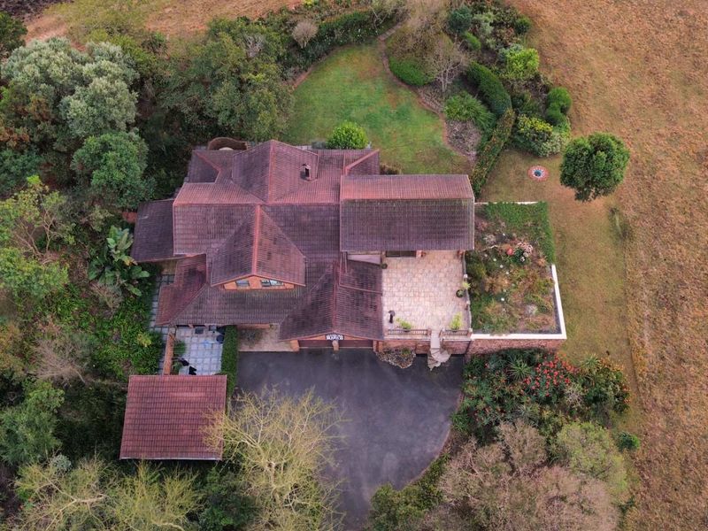 Aerial view of a residential property featuring a tiled roof, paved driveway, garage, and established landscaped gardens.