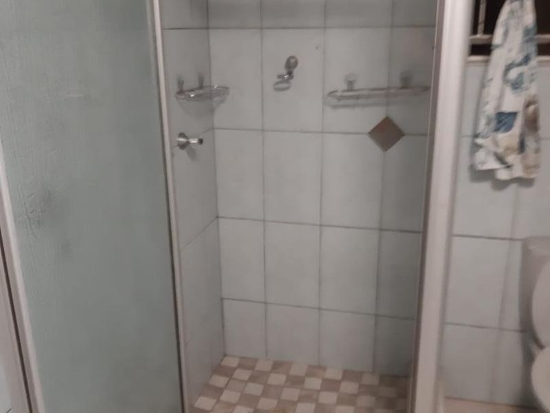 A functional bathroom shower area featuring tiled walls and flooring, currently showing signs of age and wear in the finishes.