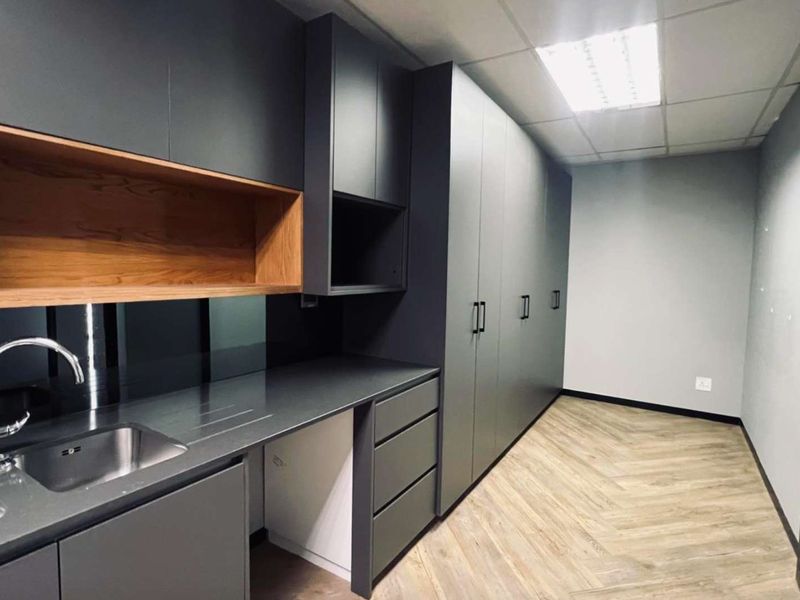 Modern office kitchenette featuring sleek dark cabinetry, integrated storage, stainless steel sink, and durable wood-look flooring.
