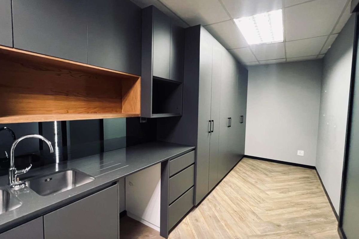 Modern office kitchenette featuring sleek dark cabinetry, integrated storage, stainless steel sink, and durable wood-look flooring.